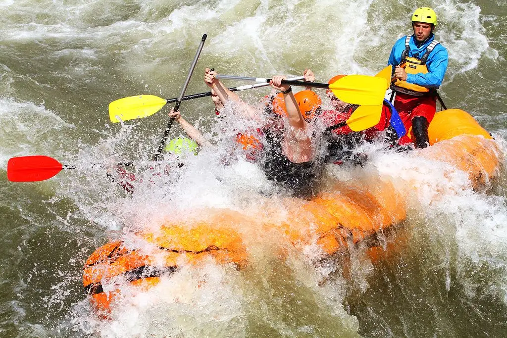 Instructor steering an orange raft through white water