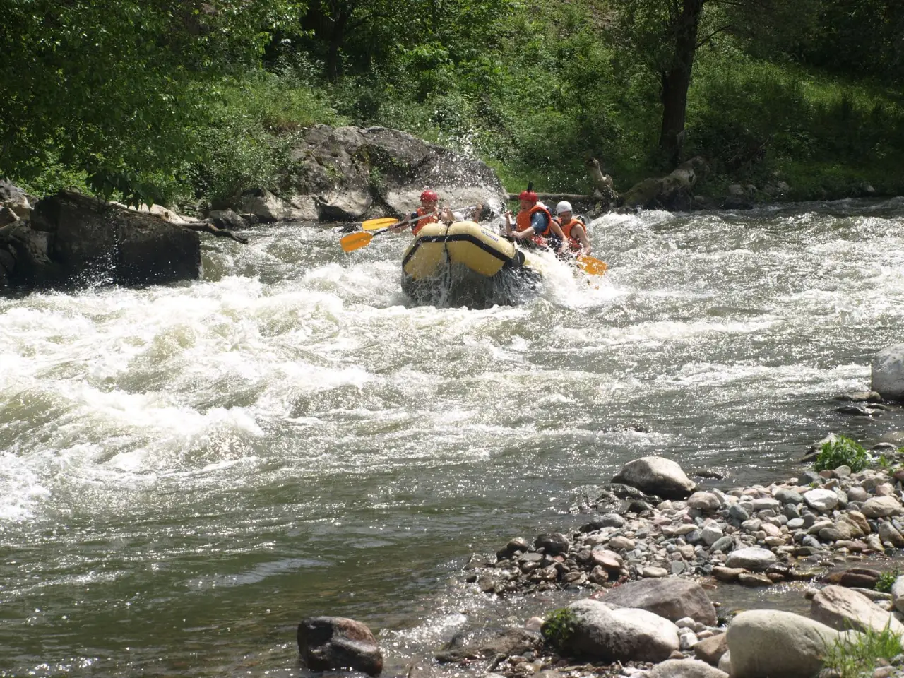 Yellow raft running a rapid between rocky banks