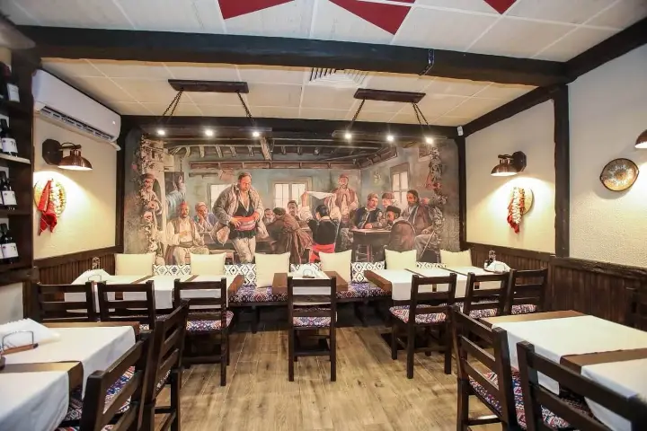 A dining room with a painted mural of village life at Izbata Tavern 2