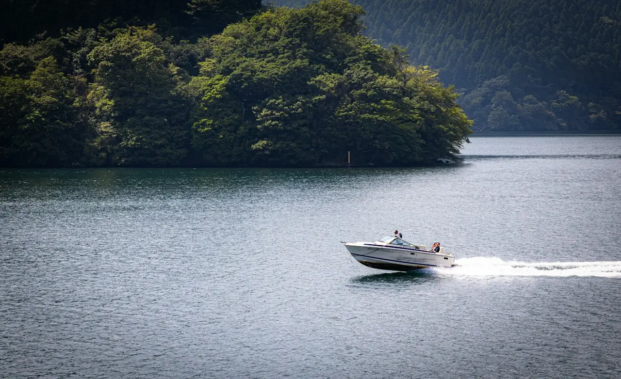 Small motorboat crossing a lake below wooded hills