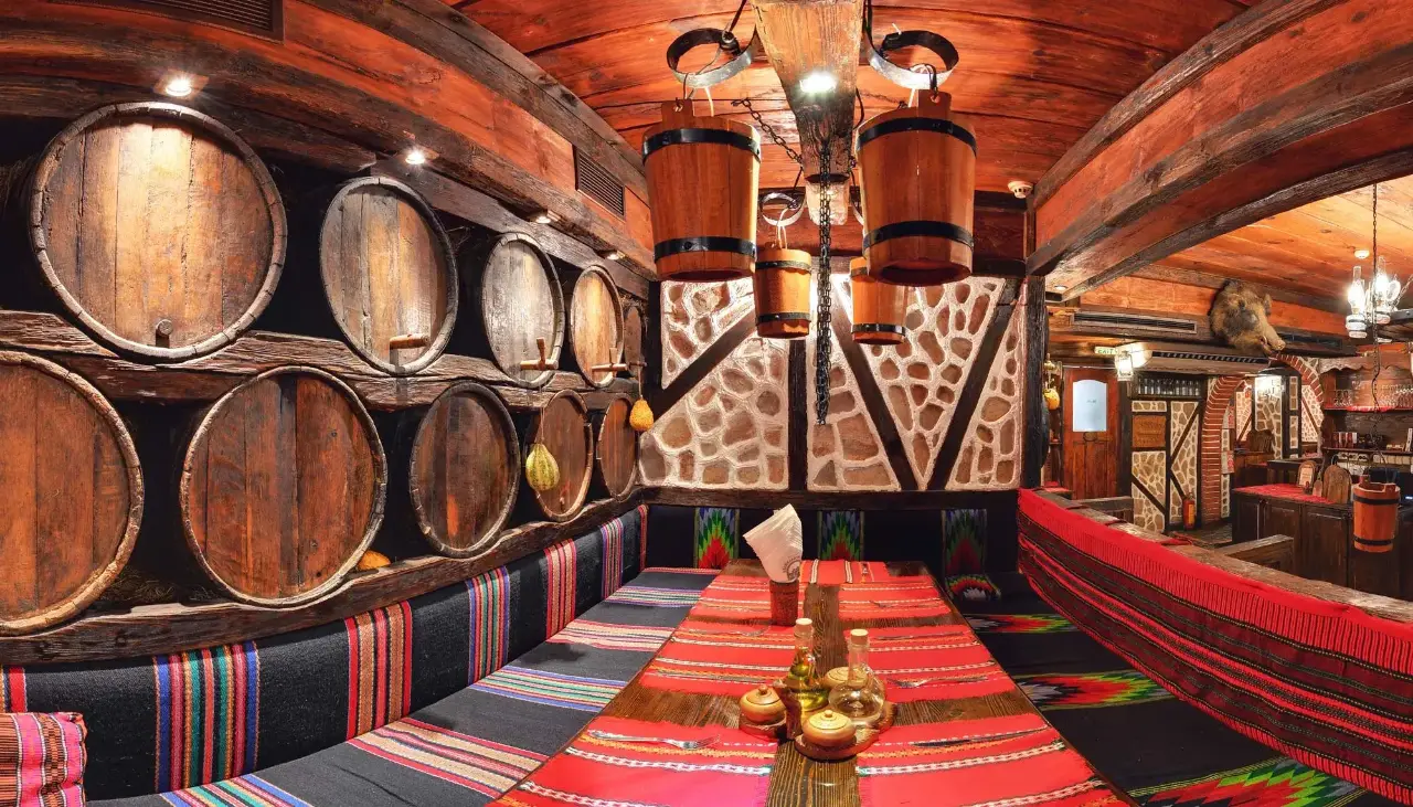 A stone wine cellar hall lined with barrels at Hadjidraganovite Izbi