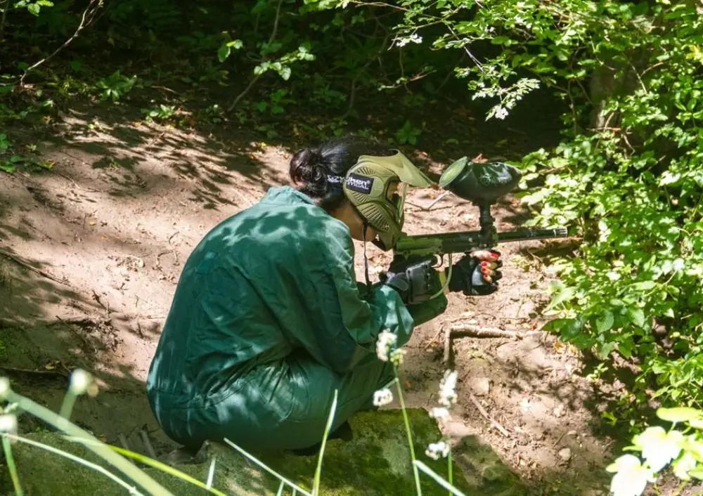 Player kneeling on a forest path with a paintball marker