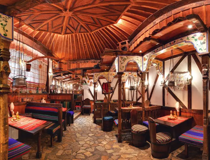 A dining hall with wooden beams and woven rugs