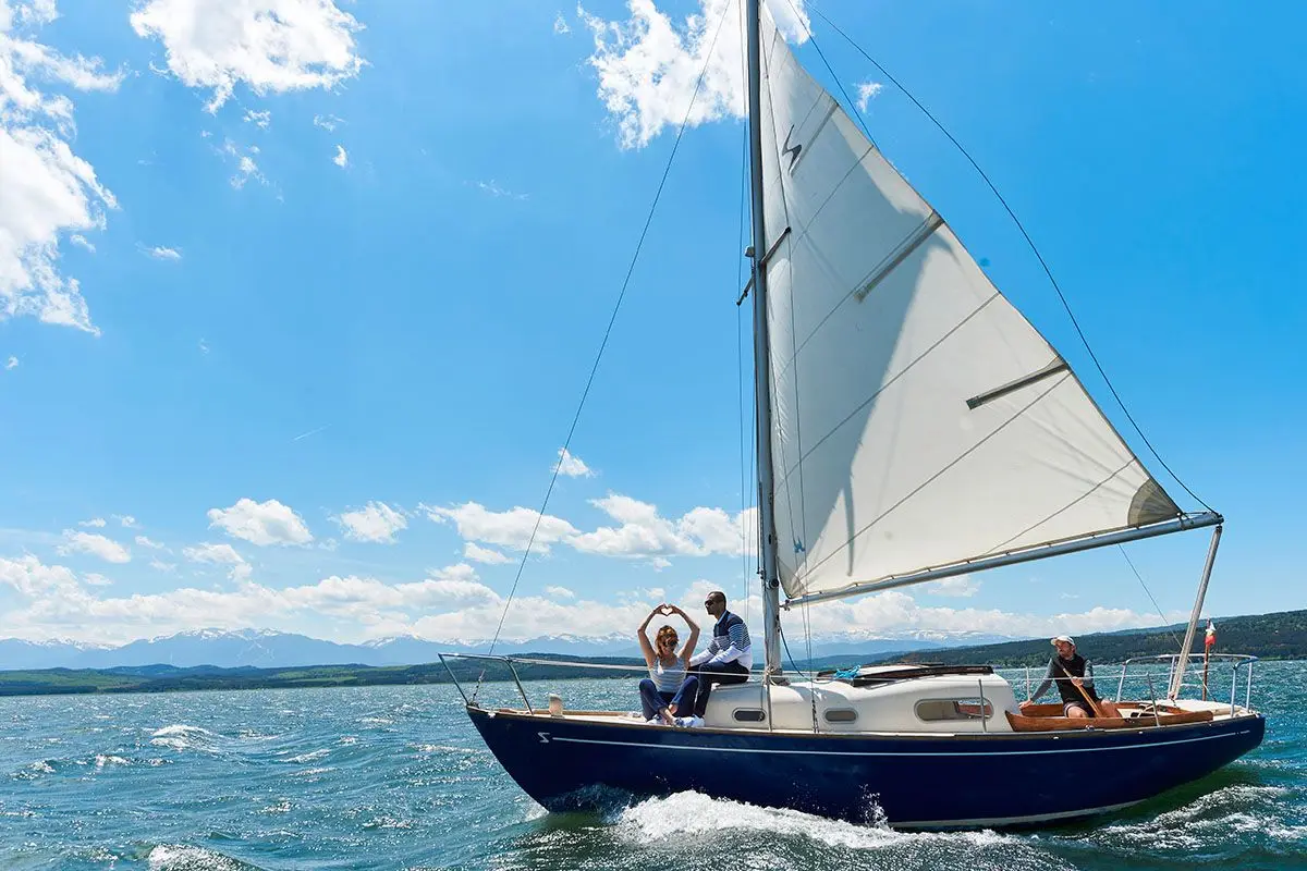 Couple waving from a blue sailing yacht on a sunny day