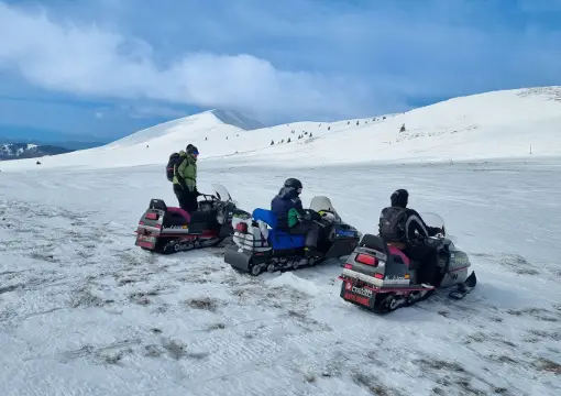 Group of snowmobiles on an open snowfield near Kom peak