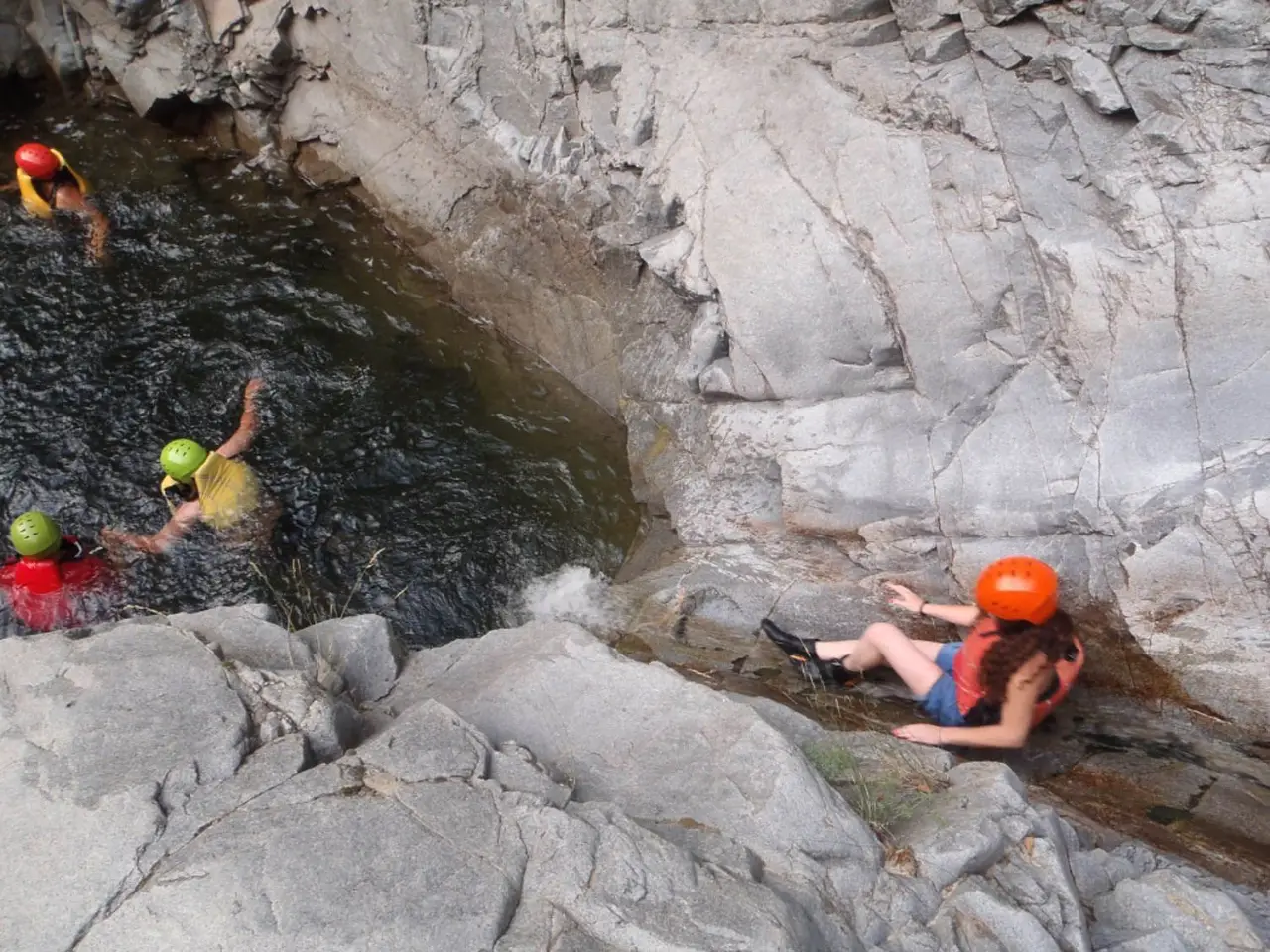 Canyoners sliding into a pool between pale rocks