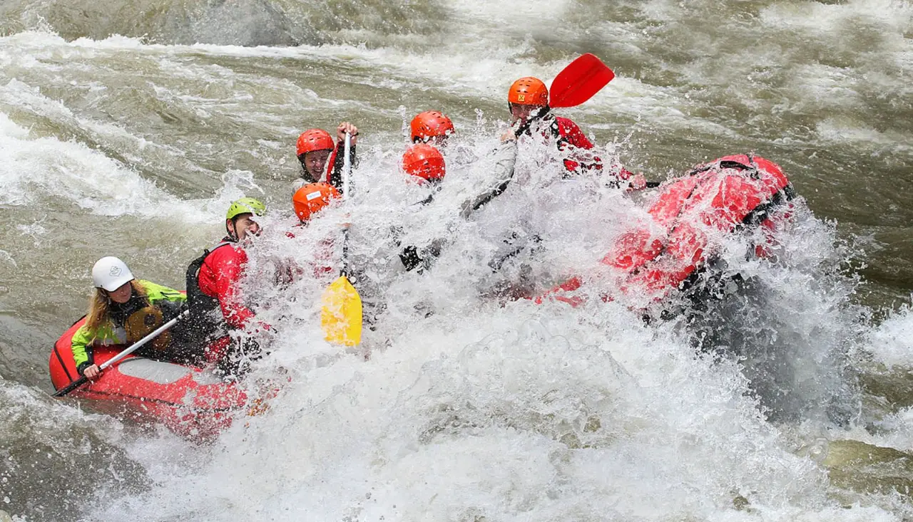 Rafters in red helmets bursting through a wave