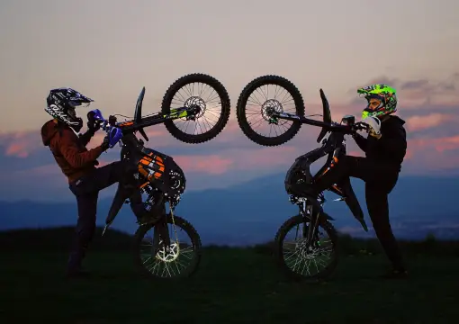Two riders lifting the front wheel of their electric motorbikes at sunset