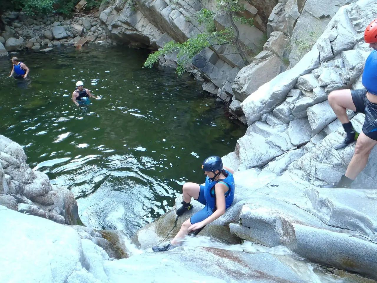 Canyoner sliding down a smooth rock chute into a green pool