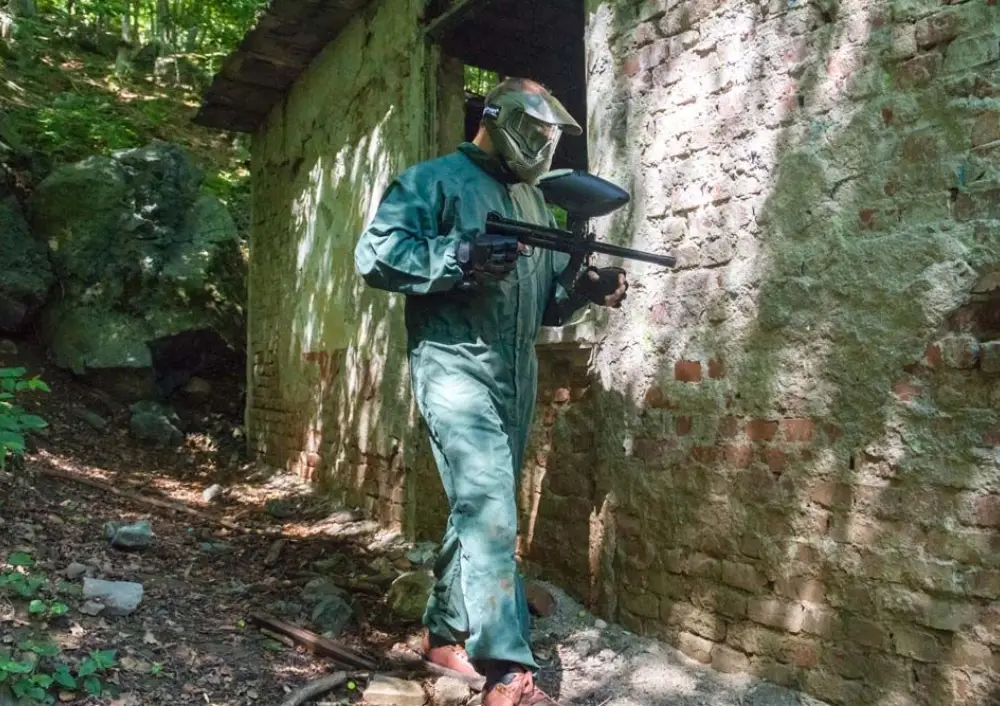 Paintball player in green overalls by a ruined brick building