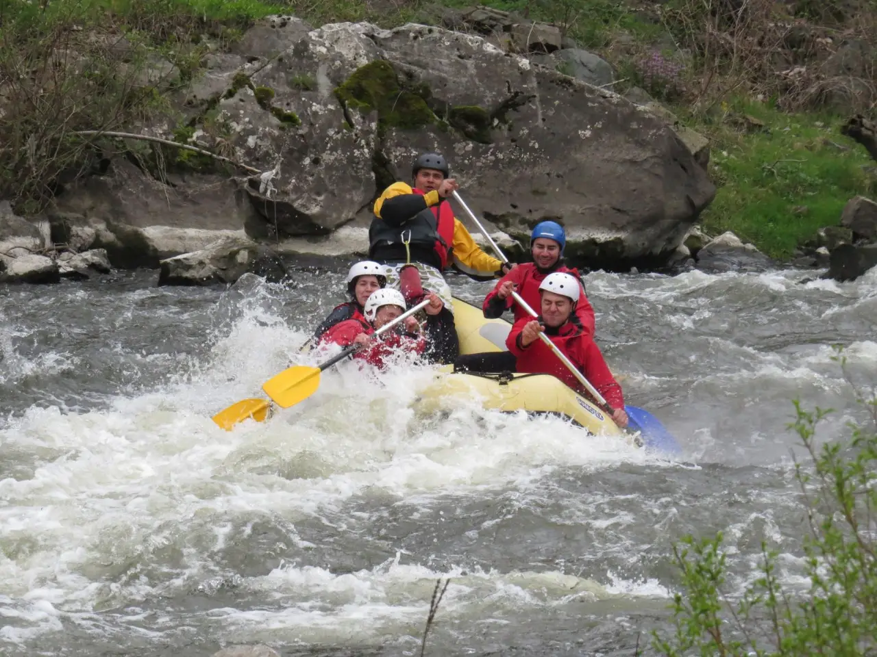 Raft splashing through white water past a large rock