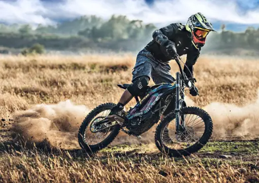 Rider on an electric dirt bike kicking up dust on a dry field