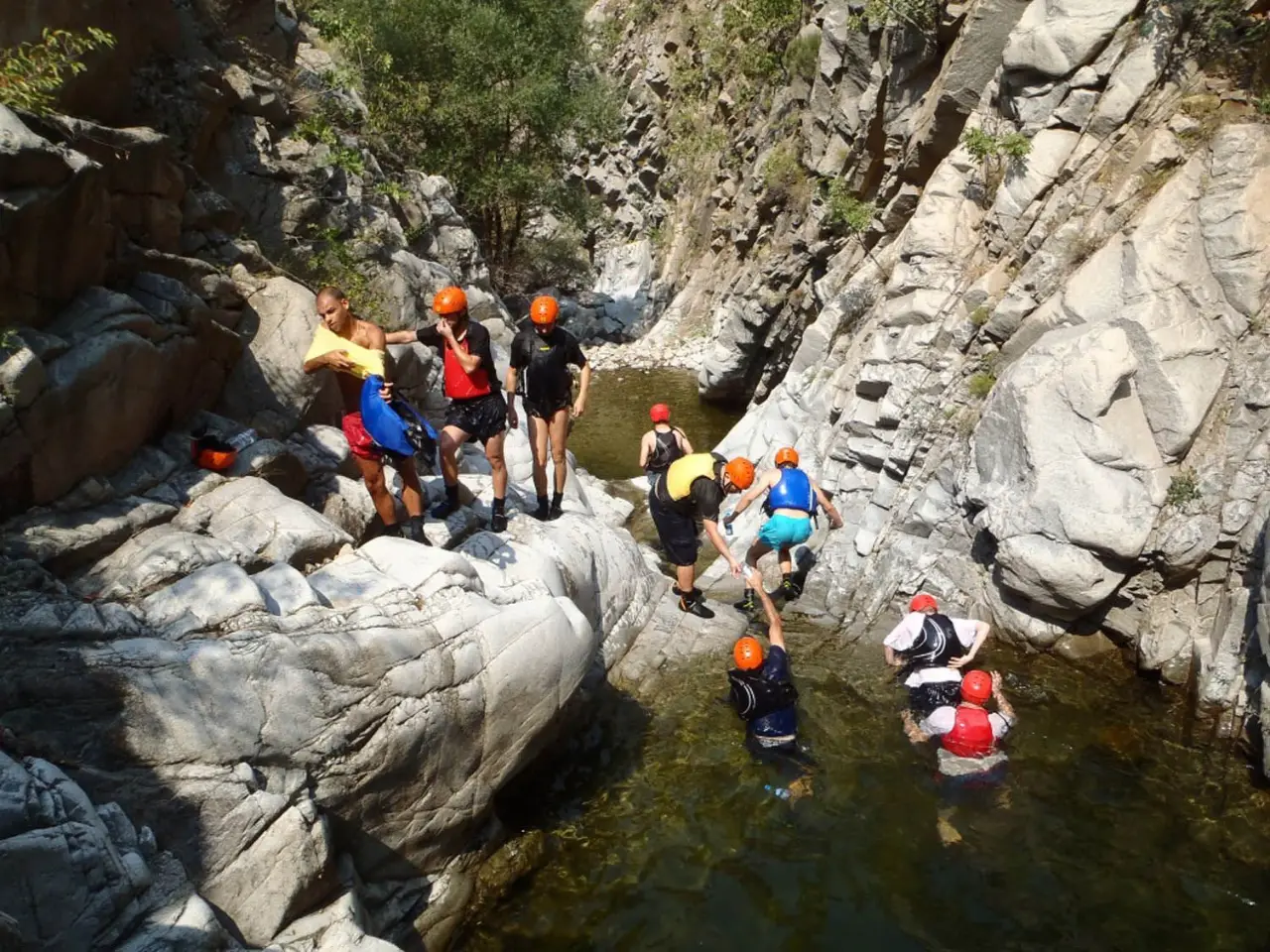 Group climbing over boulders above a deep canyon pool
